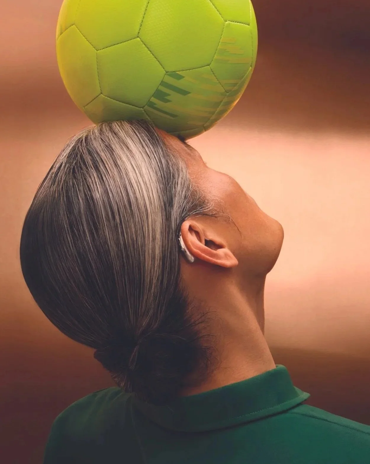 Frau mit grauen Haaren, die auf der Seite sitzt und einen grünen Ball balanciert.