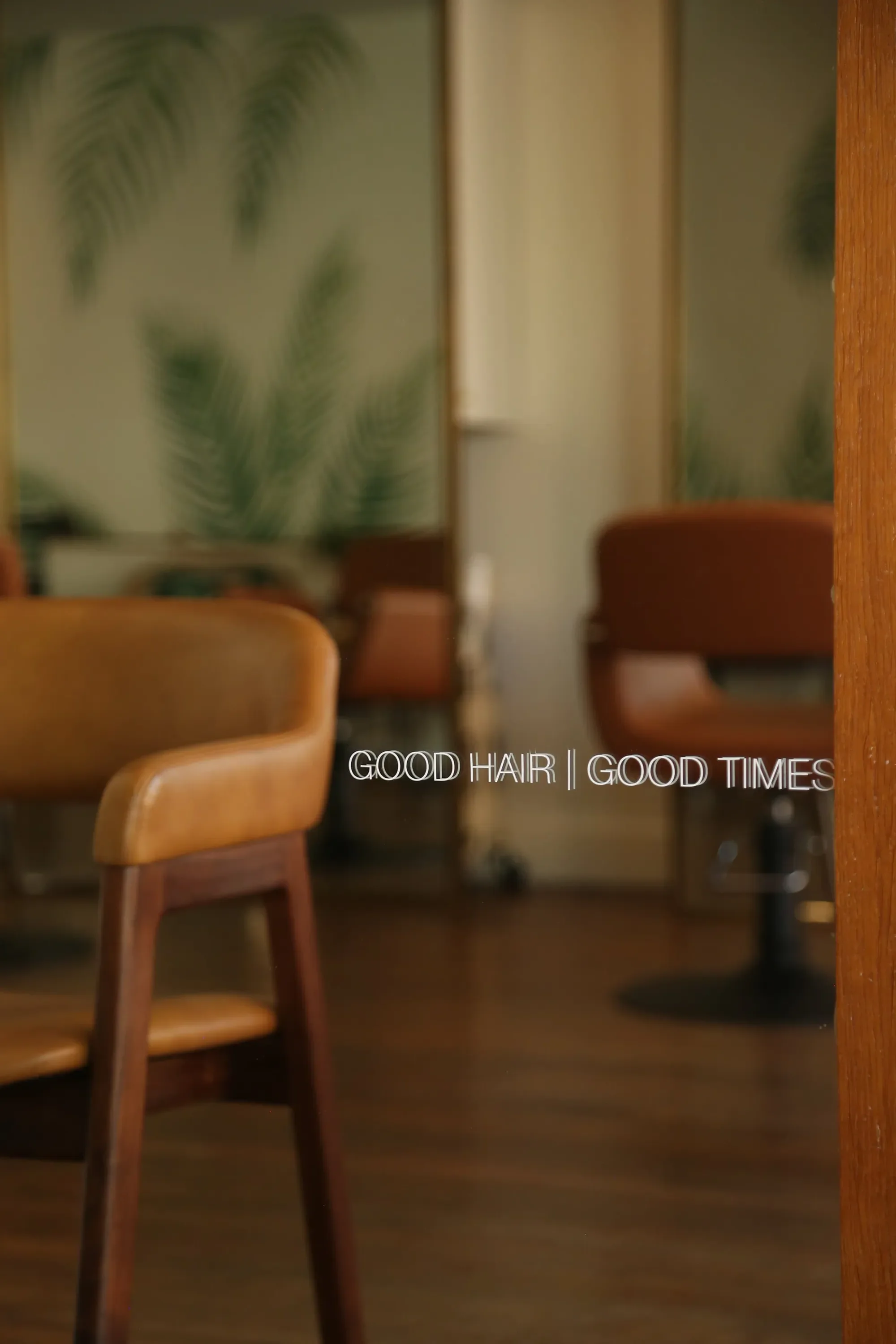 A salon with tan chairs, wooden floors, and the words GOOD HAIR | GOOD TIMES on a glass wall.