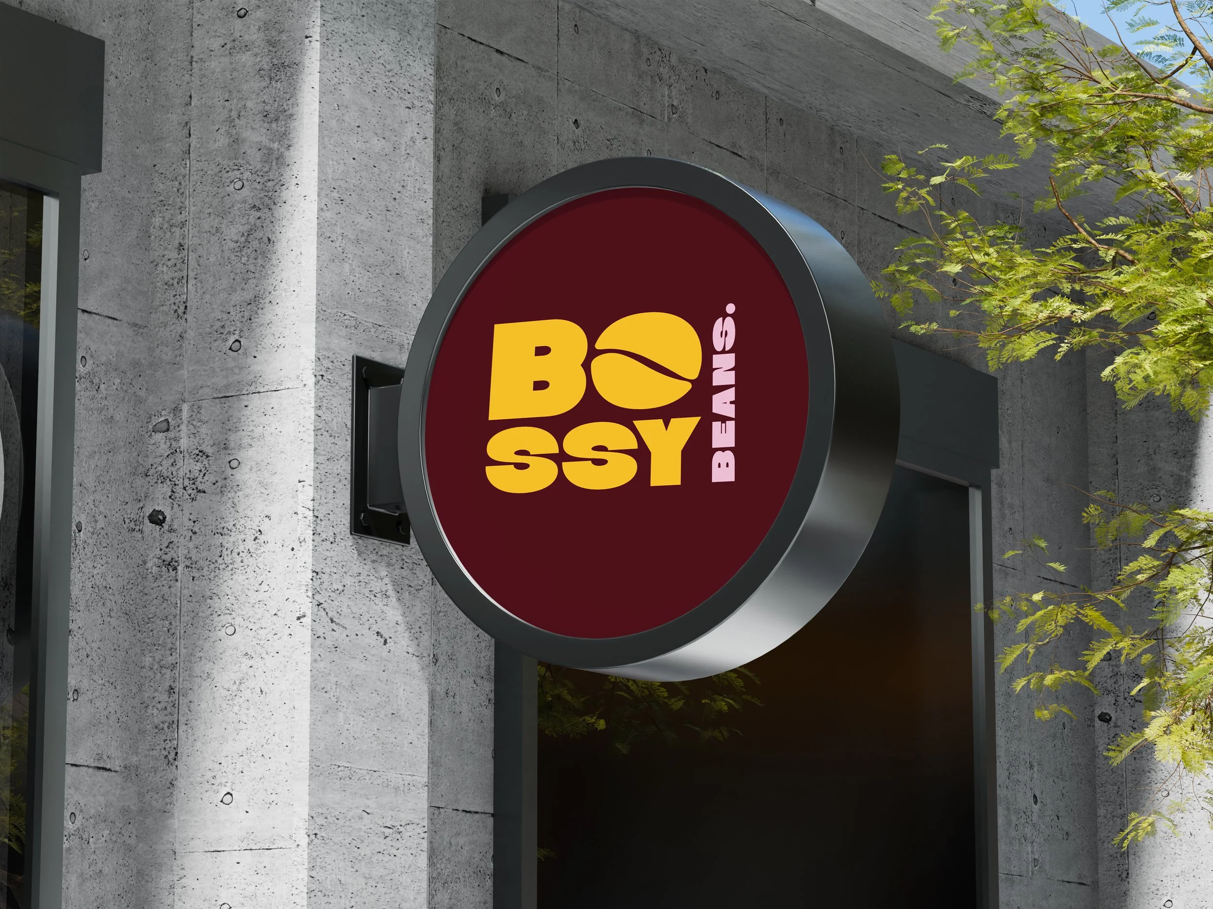 Exterior view of a BOSSY Beans store sign on a concrete wall with some green tree branches nearby.