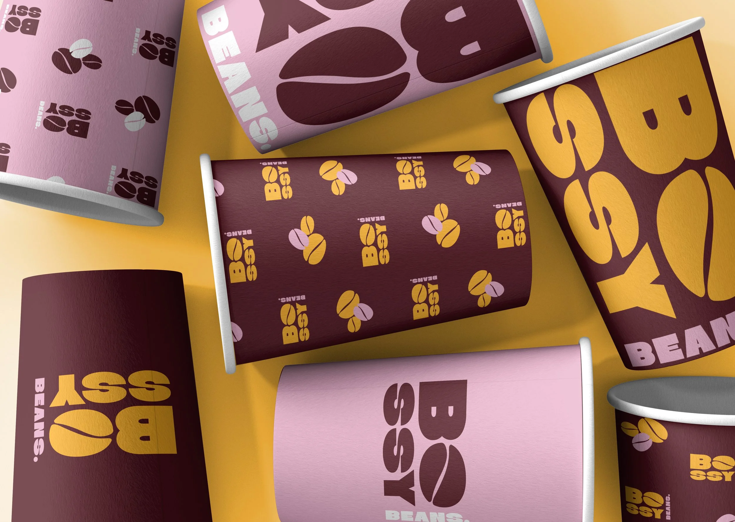 Six paper coffee cups with various bean-themed designs and colors on a yellow surface.