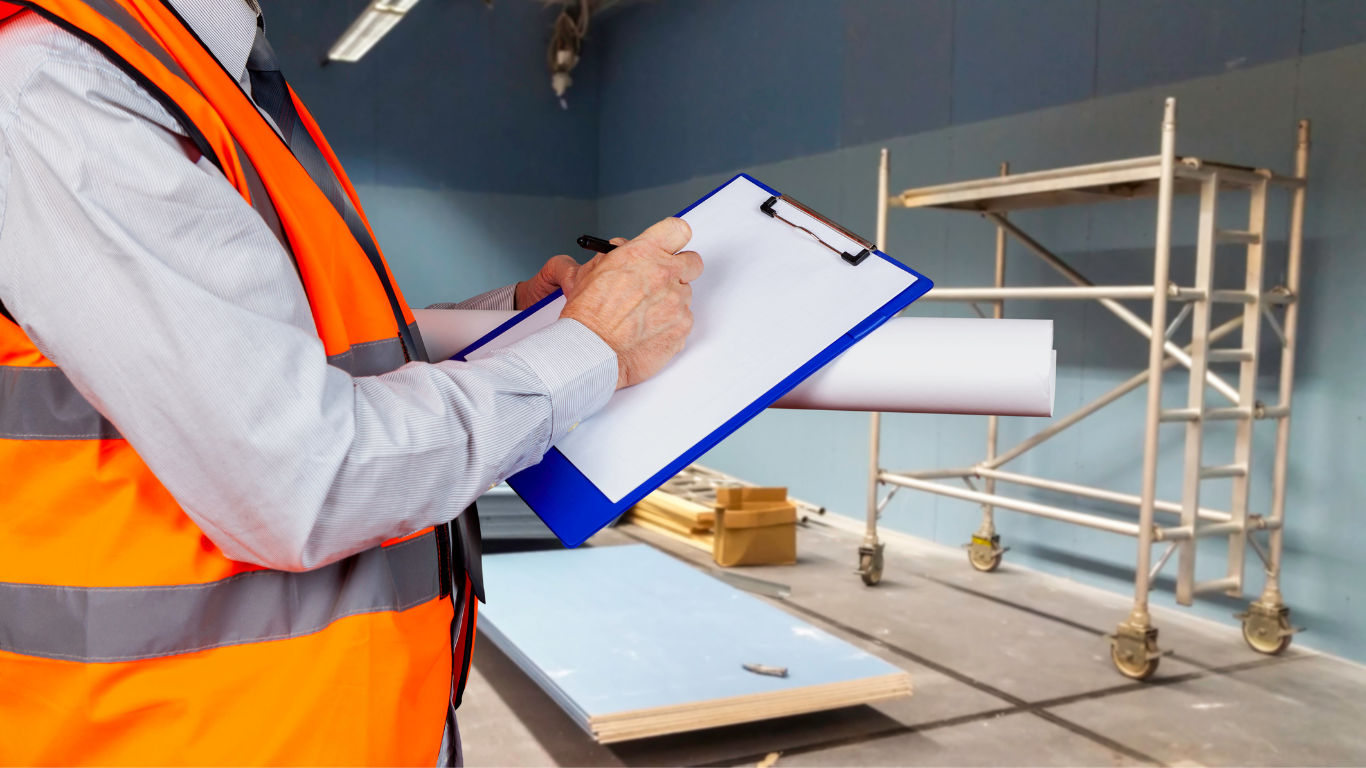Construction worker in safety vest writing on a clipboard at a construction site with scaffolding and building materials in the background.