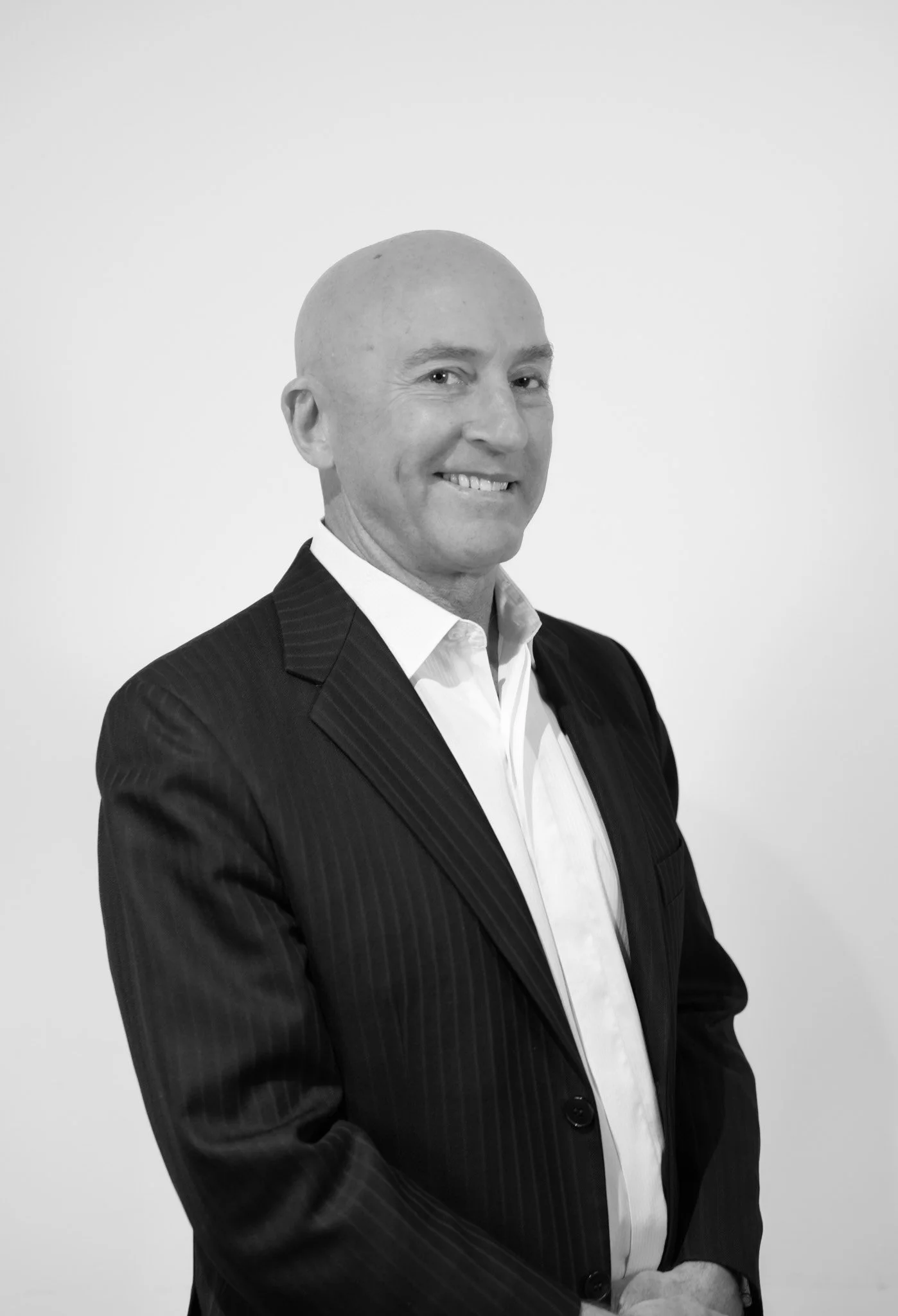 Black and white photo of a middle-aged man in a suit, smiling, standing against a plain white background.