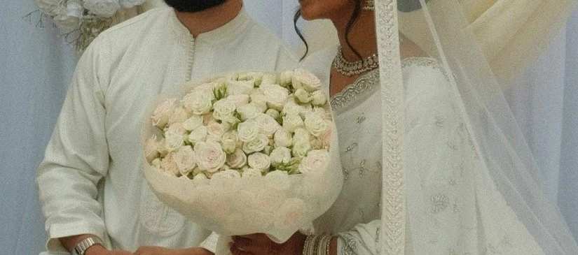 A bride and groom at their wedding ceremony, with the bride holding a bouquet of white and light pink roses