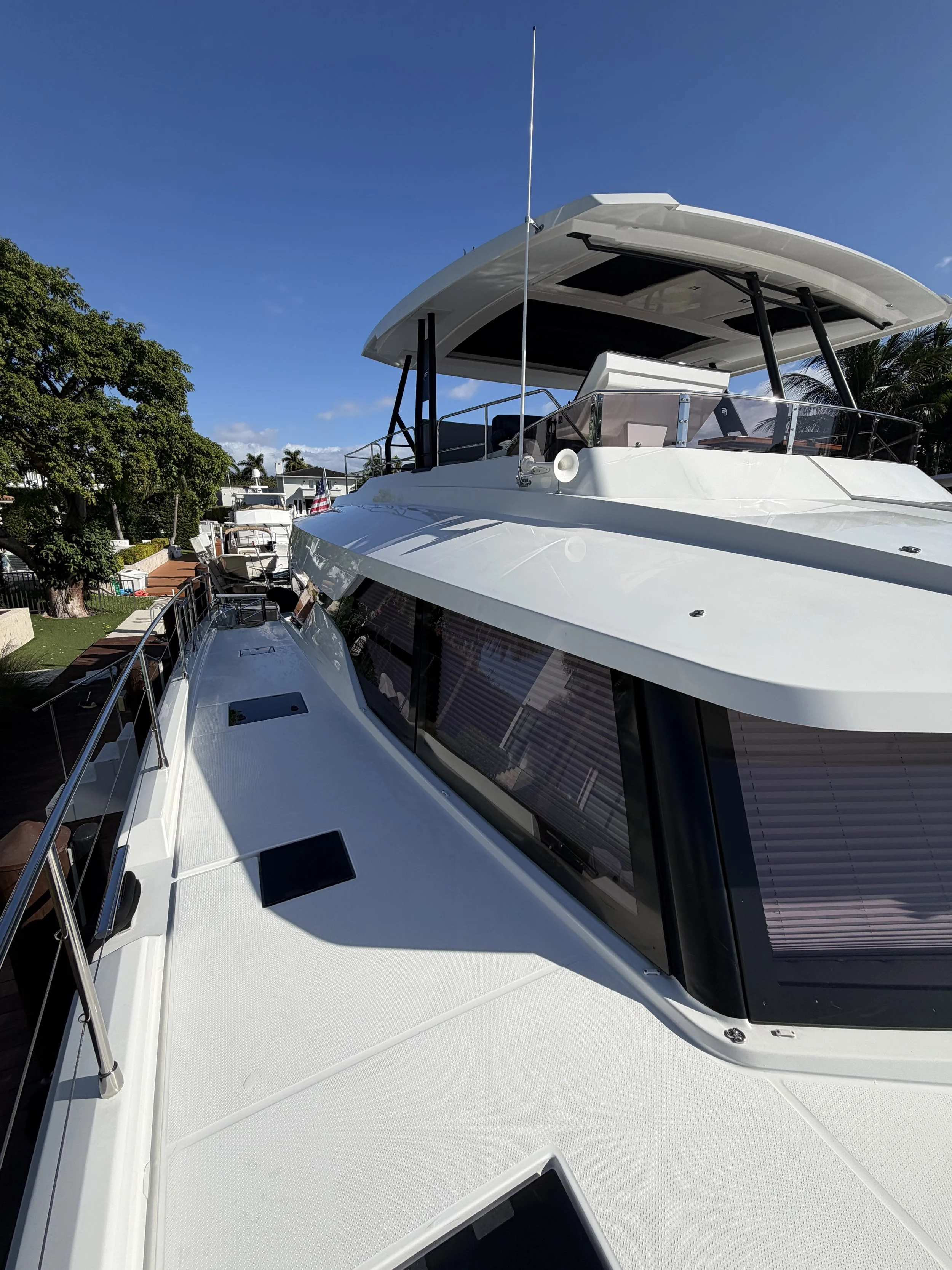 A white luxury yacht with a covered upper deck, floating in a marina with other boats in the background under a clear blue sky.