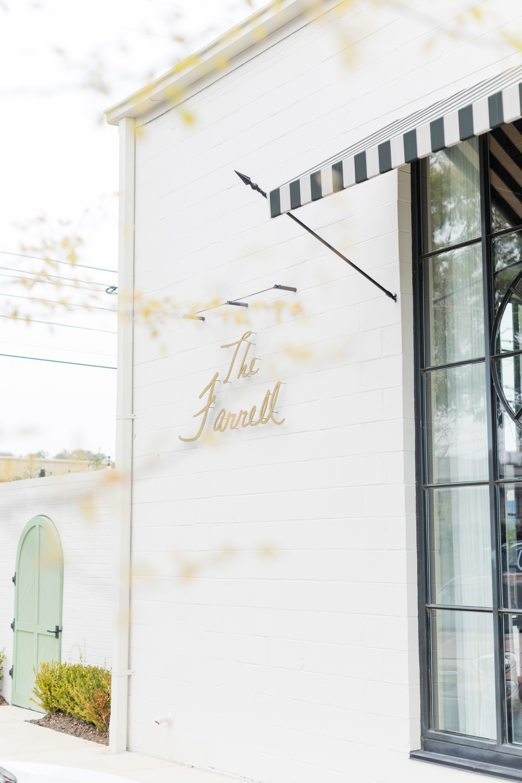 Exterior of a white building with a sign that reads 'The Farrell' and a green door, with a large window and striped awning.