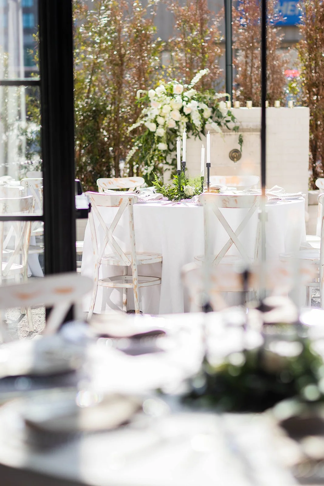 Elegant outdoor wedding reception setup with a white table, floral arrangements, and tall black candlesticks.