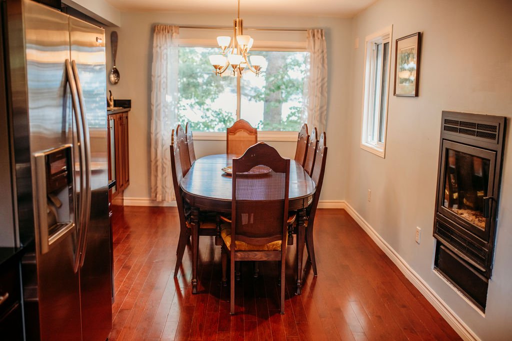 Dining room with wooden table and chairs, window with curtains, chandelier, and a wall-mounted fireplace.