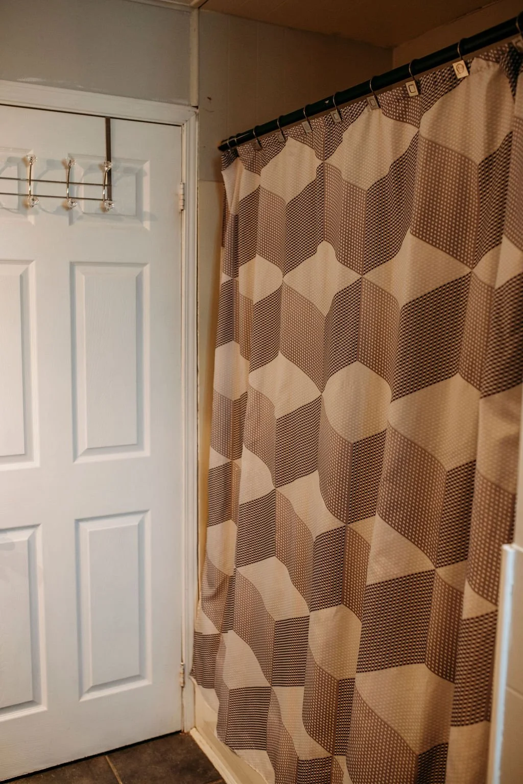 Bathroom shower with geometric patterned shower curtain in shades of beige, brown, and white.