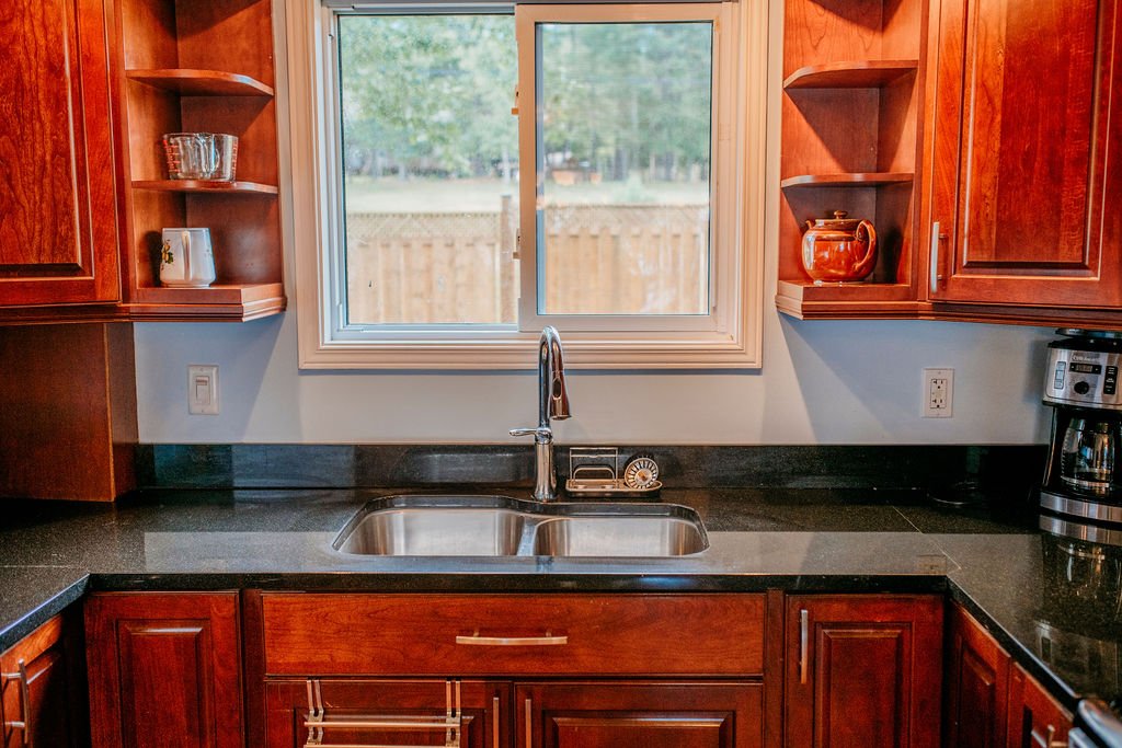 Kitchen sink with a window above, wooden cabinets on both sides, and a coffee maker on the right counter.