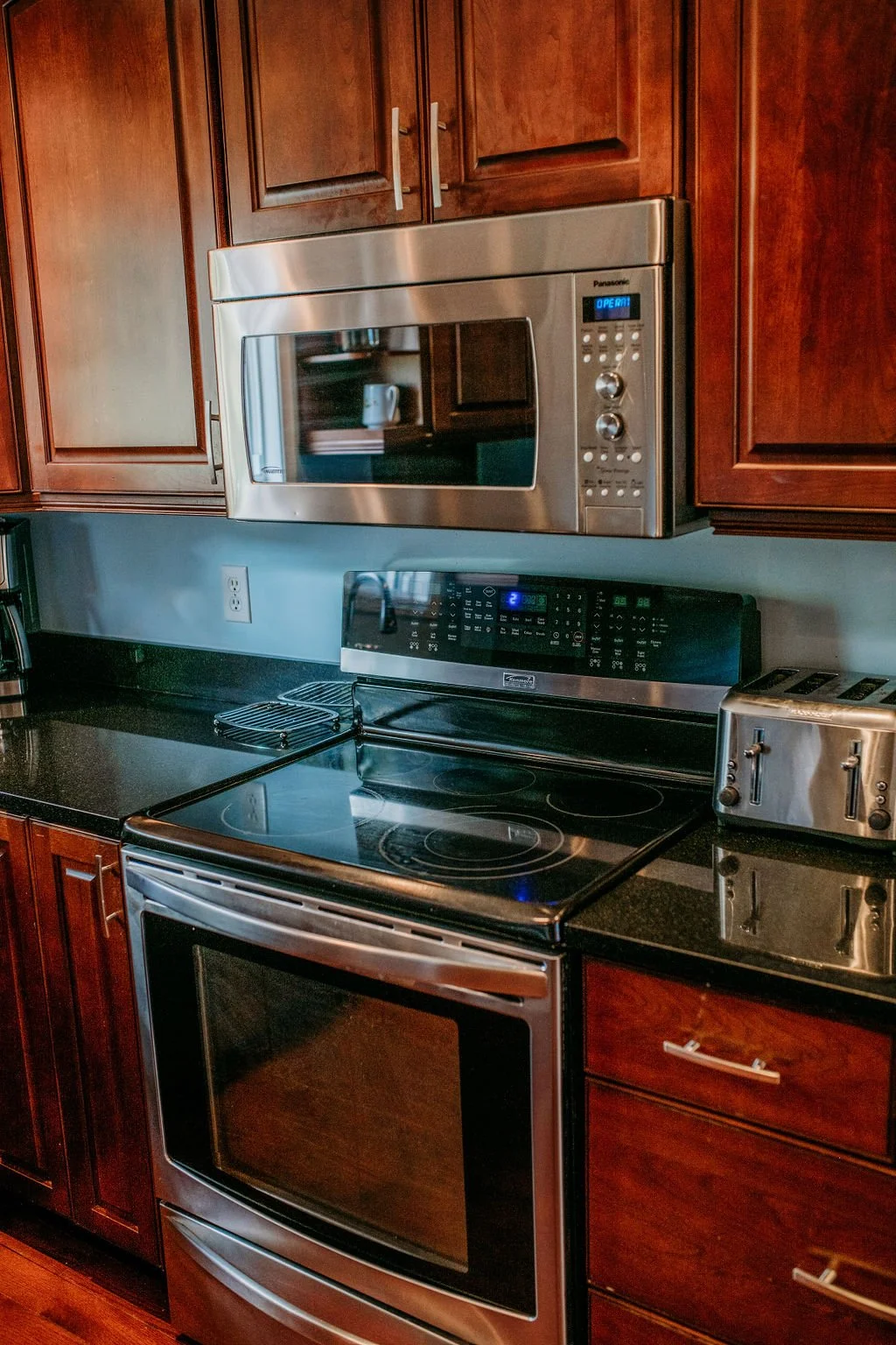 Kitchen with wood cabinets, black countertop, stainless steel microwave oven above stove, black electric stove, and toaster.