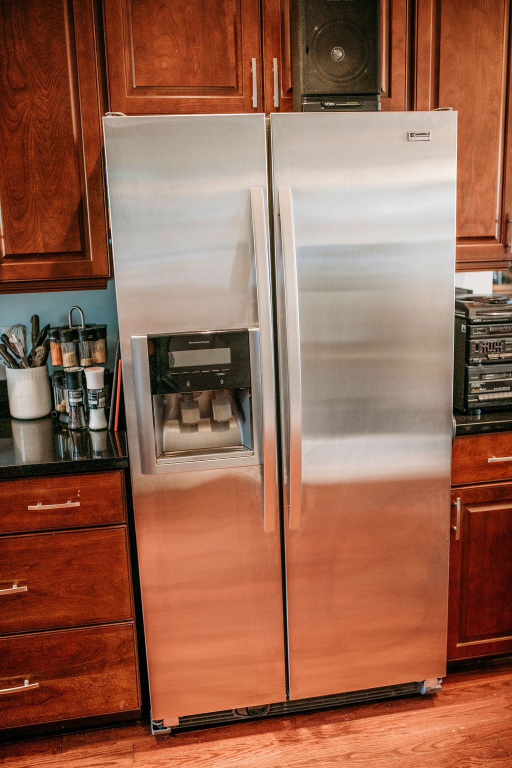Stainless steel side-by-side refrigerator with water and ice dispenser in a kitchen with wooden cabinets and drawers.