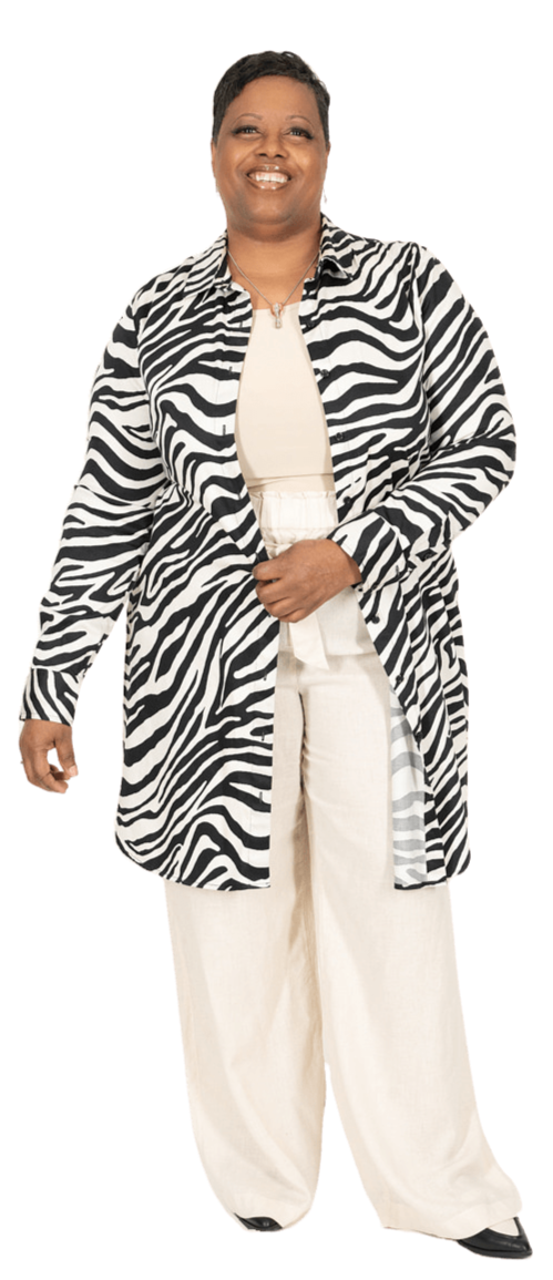 A smiling woman with short dark hair, wearing a zebra-striped coat over a beige top and off-white wide-leg pants.