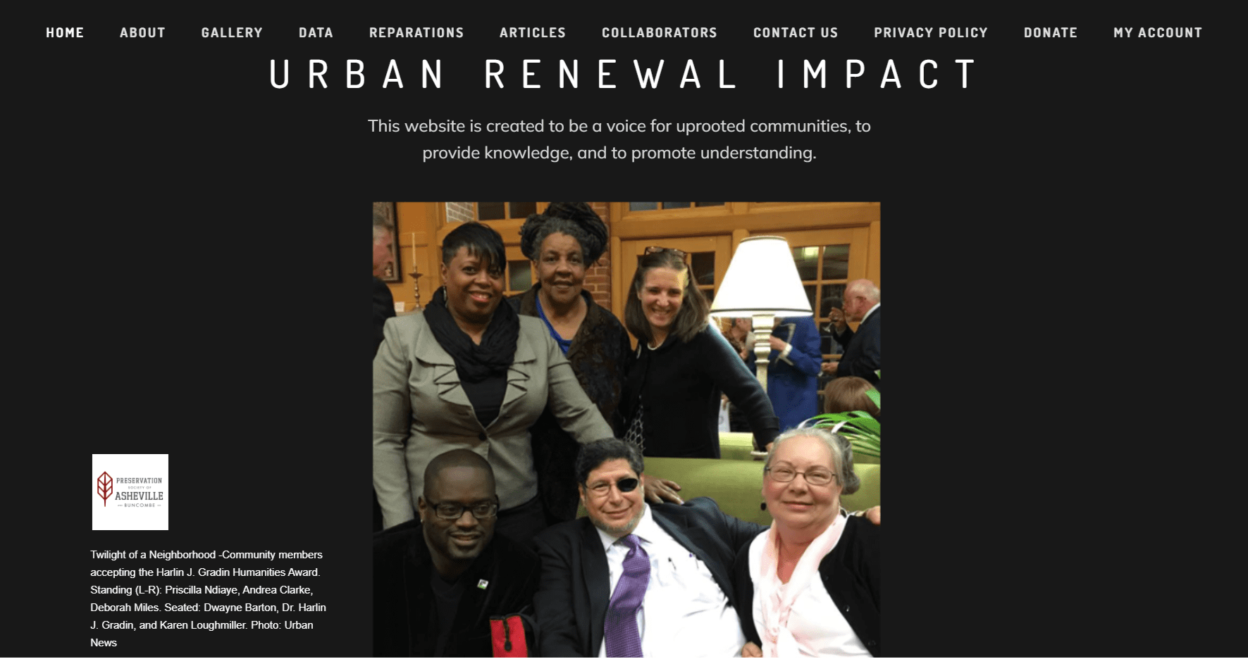 People sitting and standing together at an indoor event, with a group of five individuals smiling for the photo; background includes a lamp, wooden windows, and other attendees.