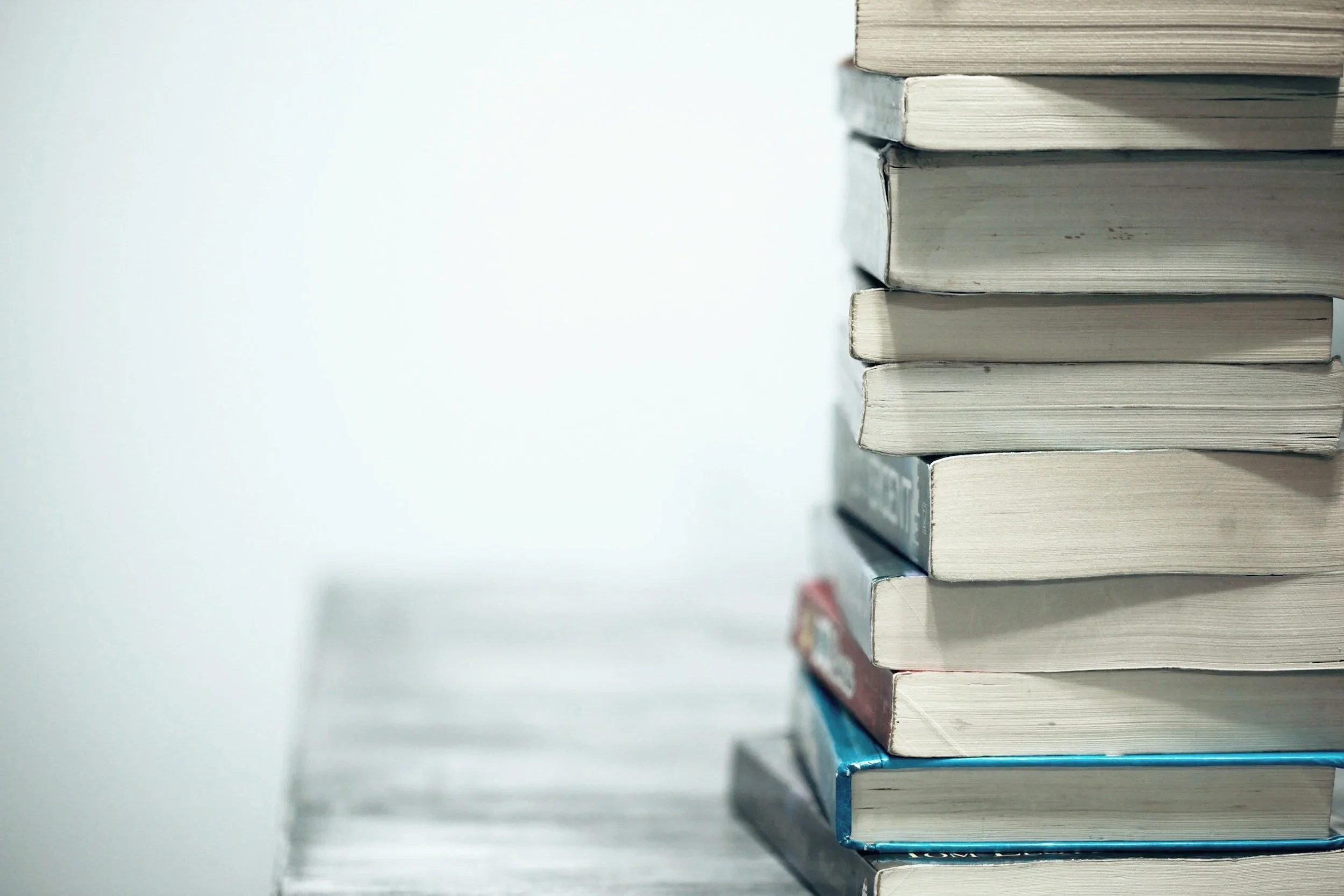 A stack of several books with worn covers, placed on a table or shelf, with a blurred background.