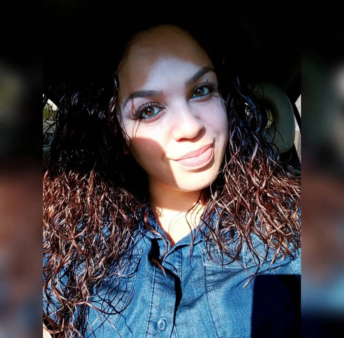 Close-up photo of a young woman with curly brown hair and brown eyes, smiling, in a car with sunlight on her face. A happy Luna & Soul client.