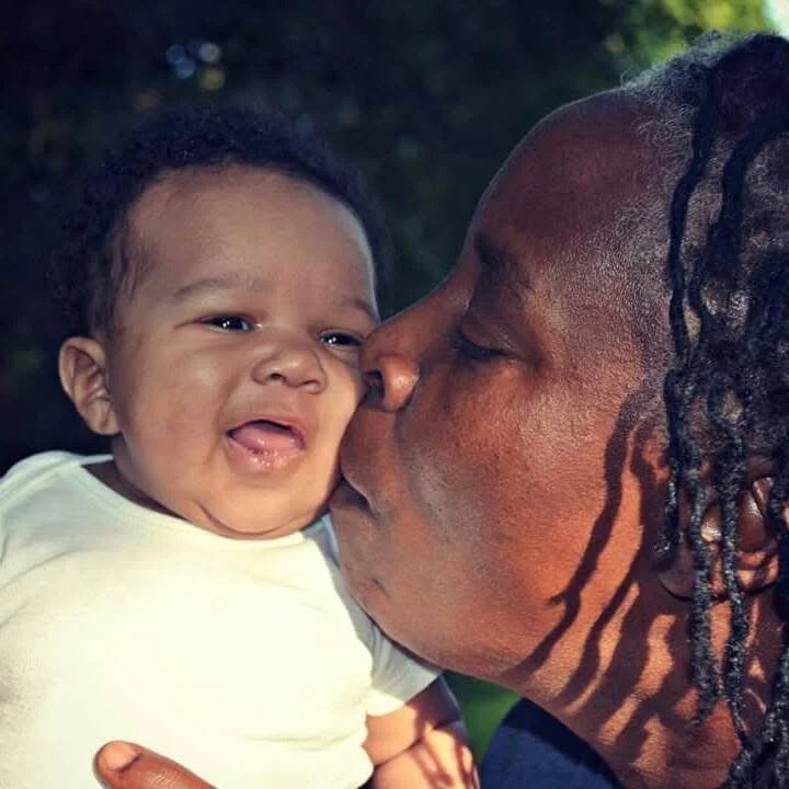 A woman is kissing a smiling baby boy on the cheek outdoors. happy Luna & Soul clients. 