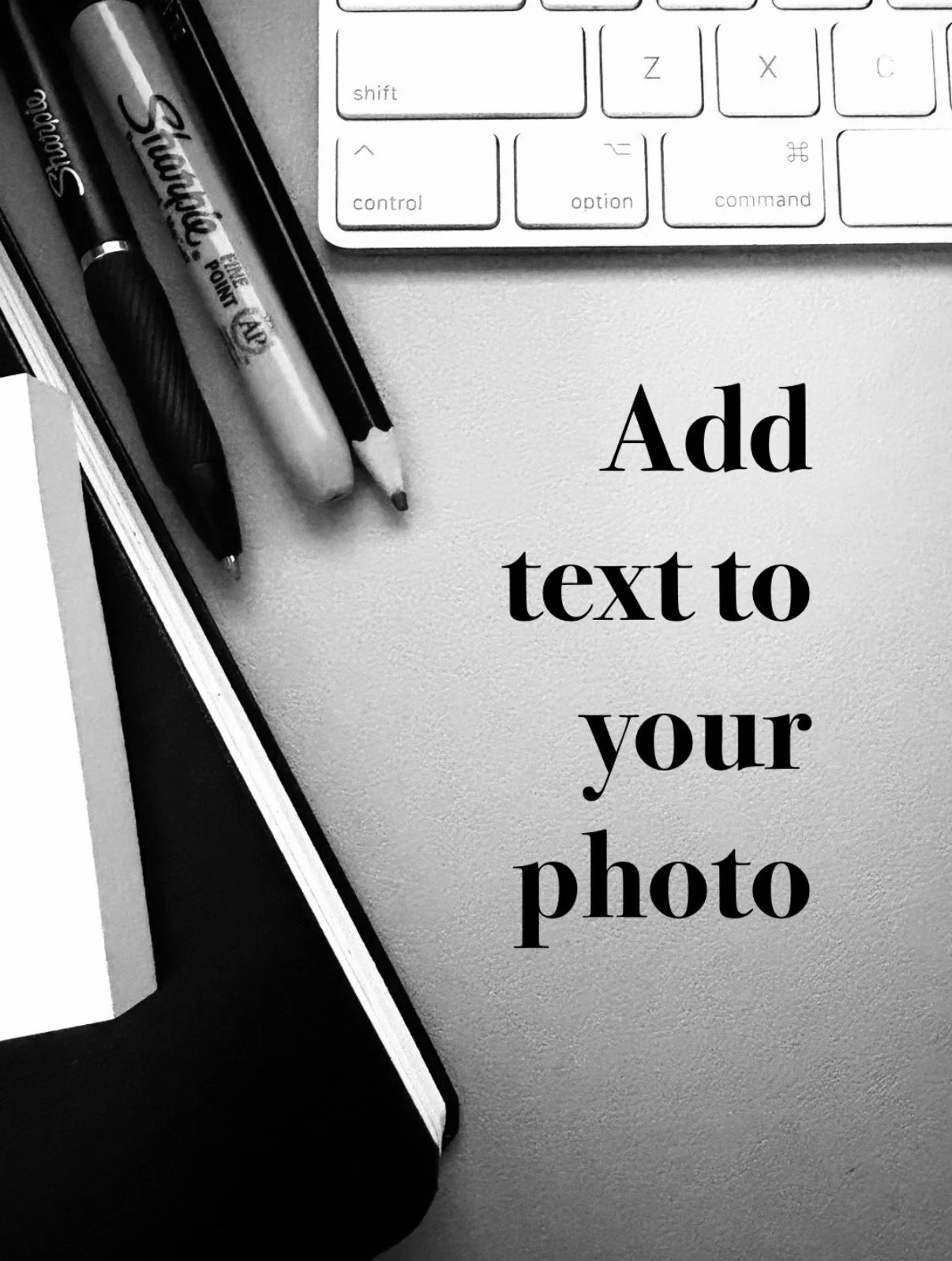 "Add text to your photo" bold serif text added on a photo of a desk top with keyboard, pencil, sharpie marker, sharpie pen, notebook, and stick notes surrounding the text