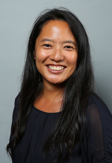 A headshot of an Asian woman with long black hair, smiling warmly at the camera, wearing a black shirt