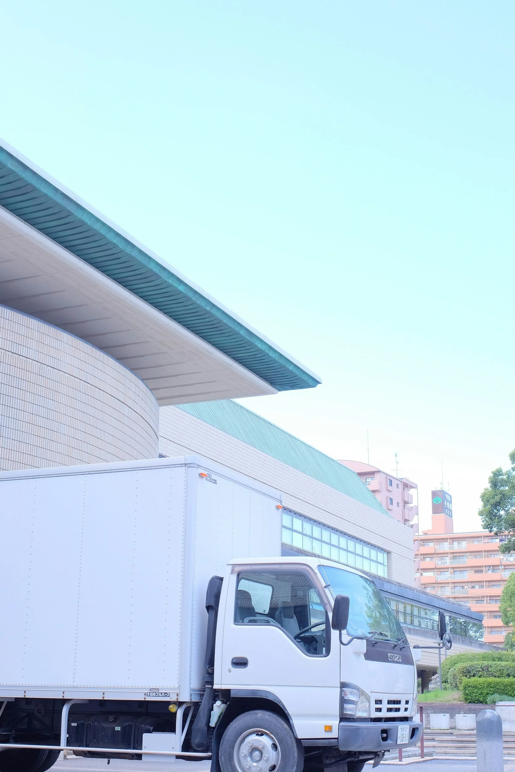 White delivery truck parked in front of a modern building with curved architectural design, under a clear blue sky.