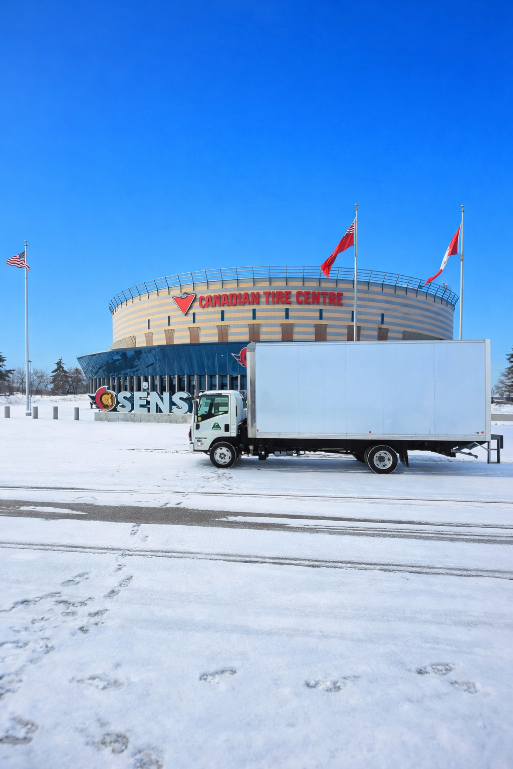 A delivery truck parked in front of the Canadian Tire Centre, which is a large sports and entertainment arena. The arena has a sign and flags, and the ground is covered in snow with footprints and tire tracks.