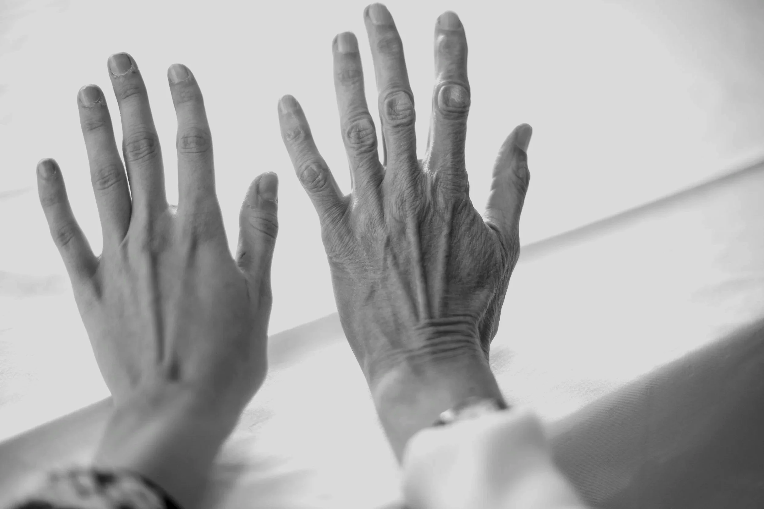 Two adult hands, one older and one younger, placed side by side on a flat surface, photographed in black and white.