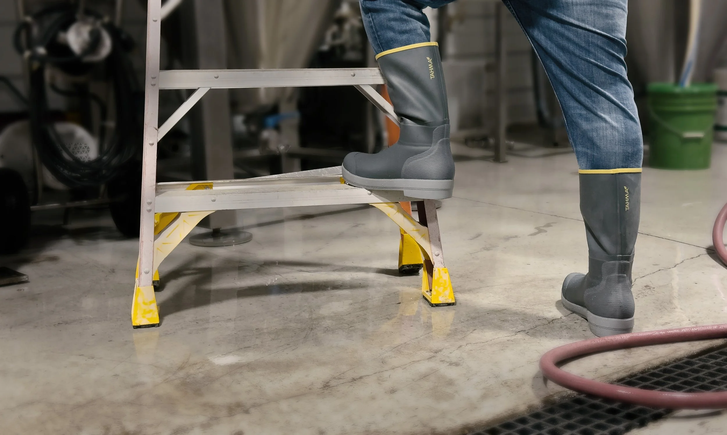 Tahma tall boots standing on wet floor and one foot on a ladder at industrial facility