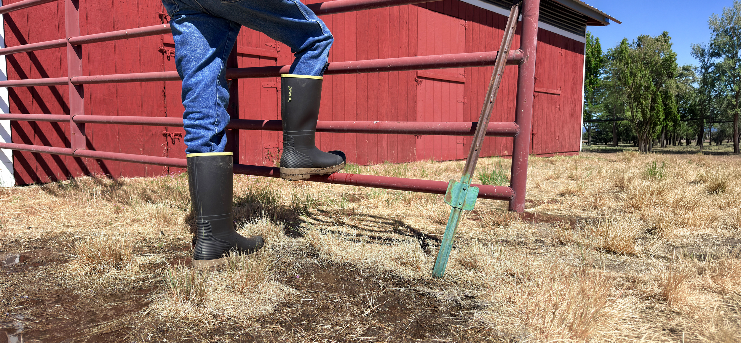 Farmer wearing Tahma All Terrain boots standing in front of a redbird with one foot on a gate