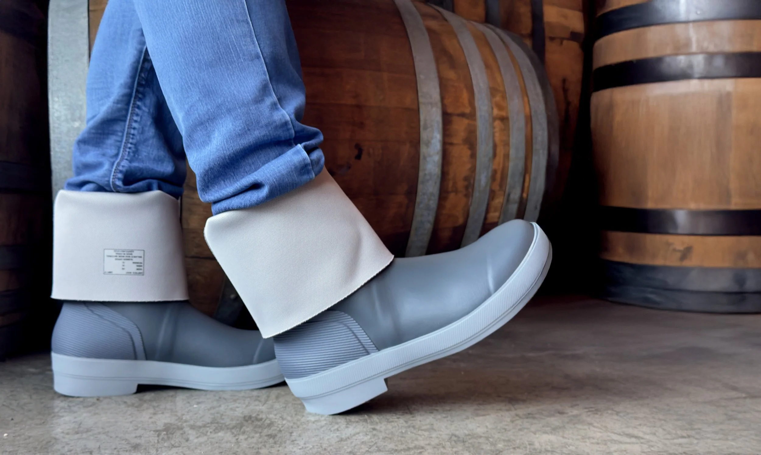 Worker at a winery wearing tall Tahma boots rolled down standing in front of wine barrels