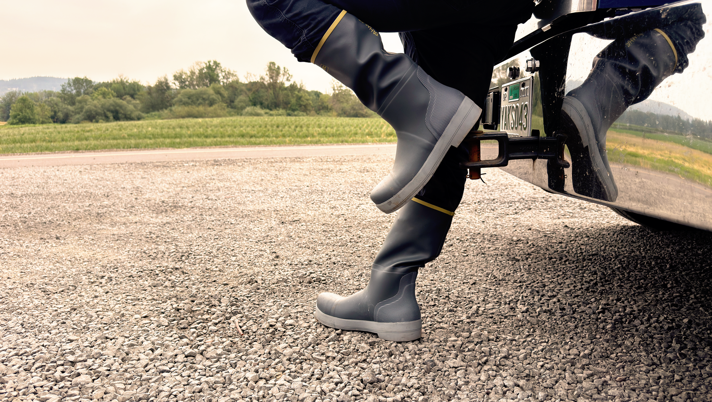 Tahma 15 inch tall boots worn by a trucker standing in from of his rig with a gravel road and field in the background