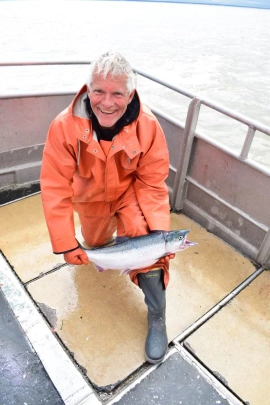 Commercial fisherman wearing tall Tahma boots holding a fish on a commercial fishing boat