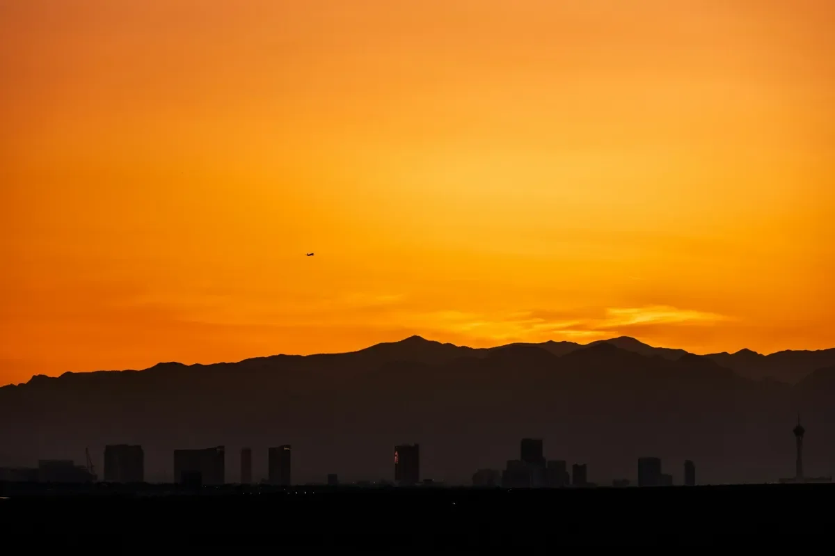 Las Vegas skyline at sunrise with mountains in the background and a warm orange sky.