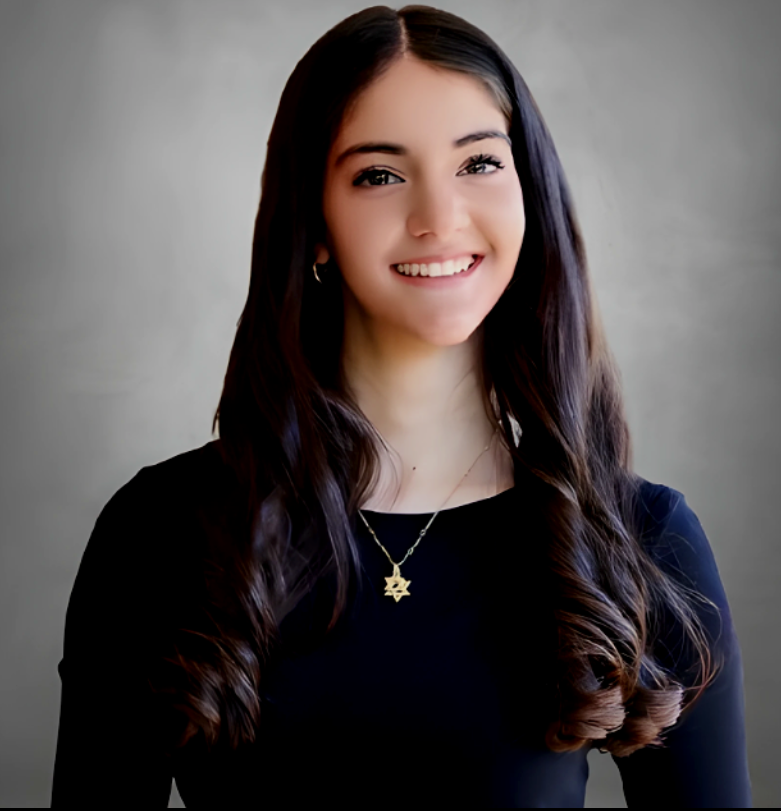 A young woman with long dark hair, smiling, wearing a black top and a gold star necklace, posing against a plain background.