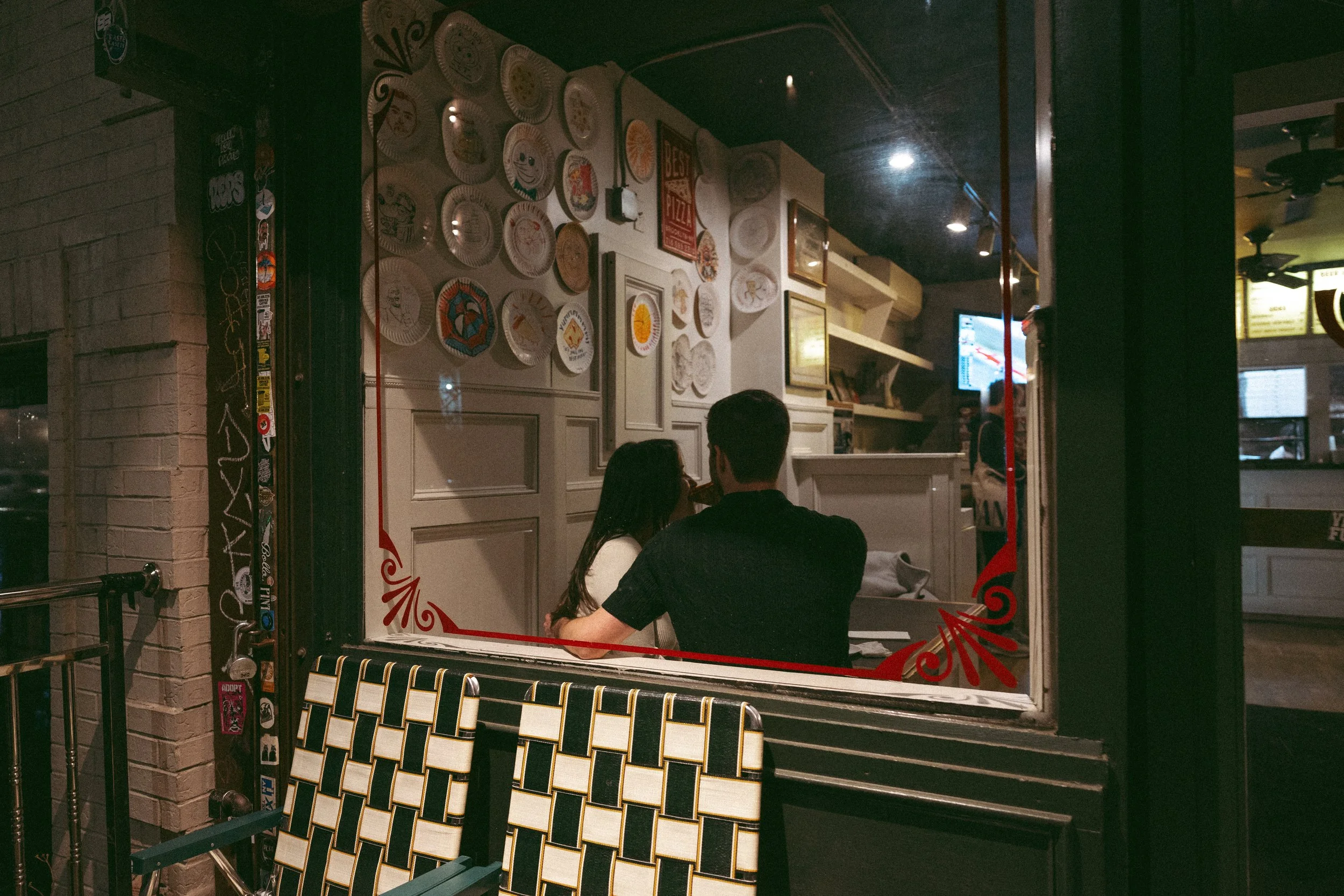 Couple dining at a restaurant seen through a window decorated with red trim and stickers.