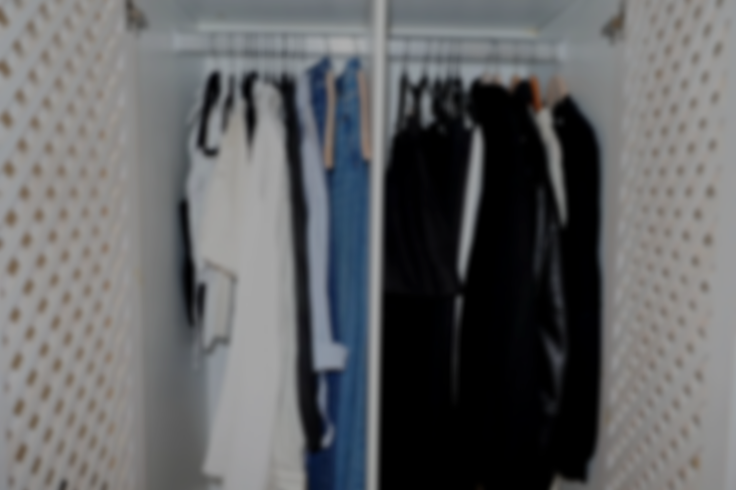 Blurred closet with hanging clothes, including shirts, pants, and jackets on hangers.