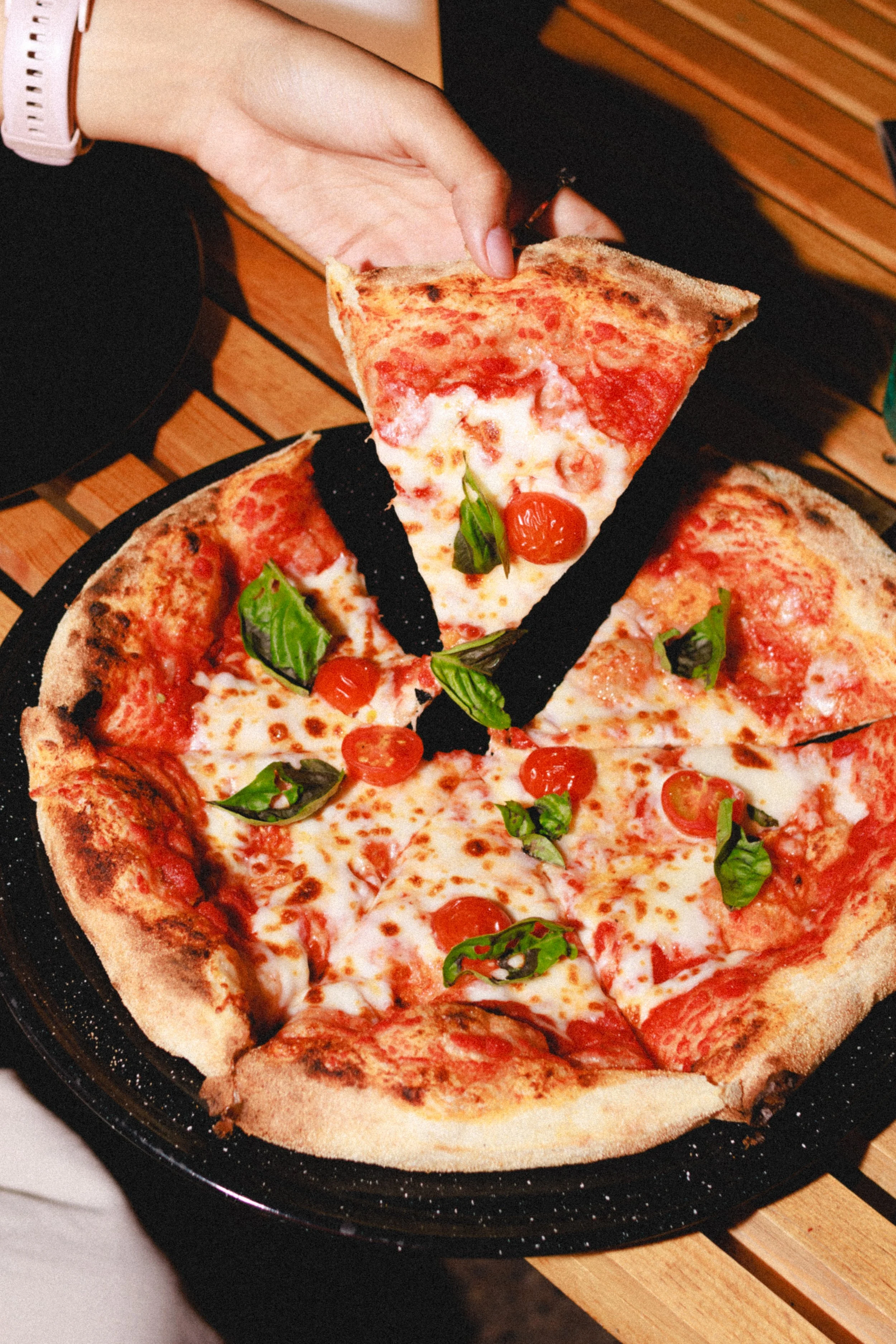 Persona sirviendo una porción de pizza de queso, tomate y albahaca sobre un plato negro.