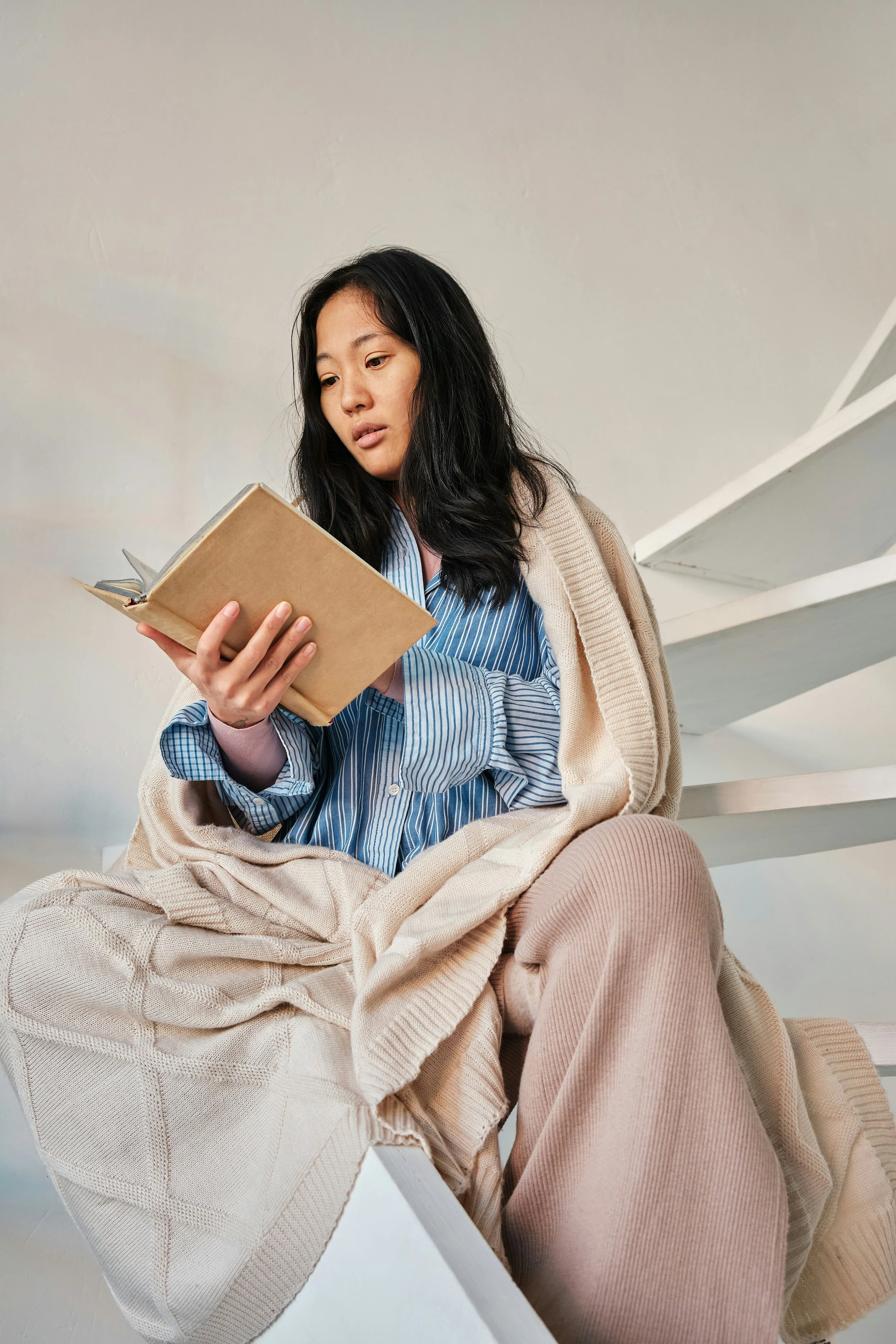 a person wrapped in blankets sitting down reading a book
