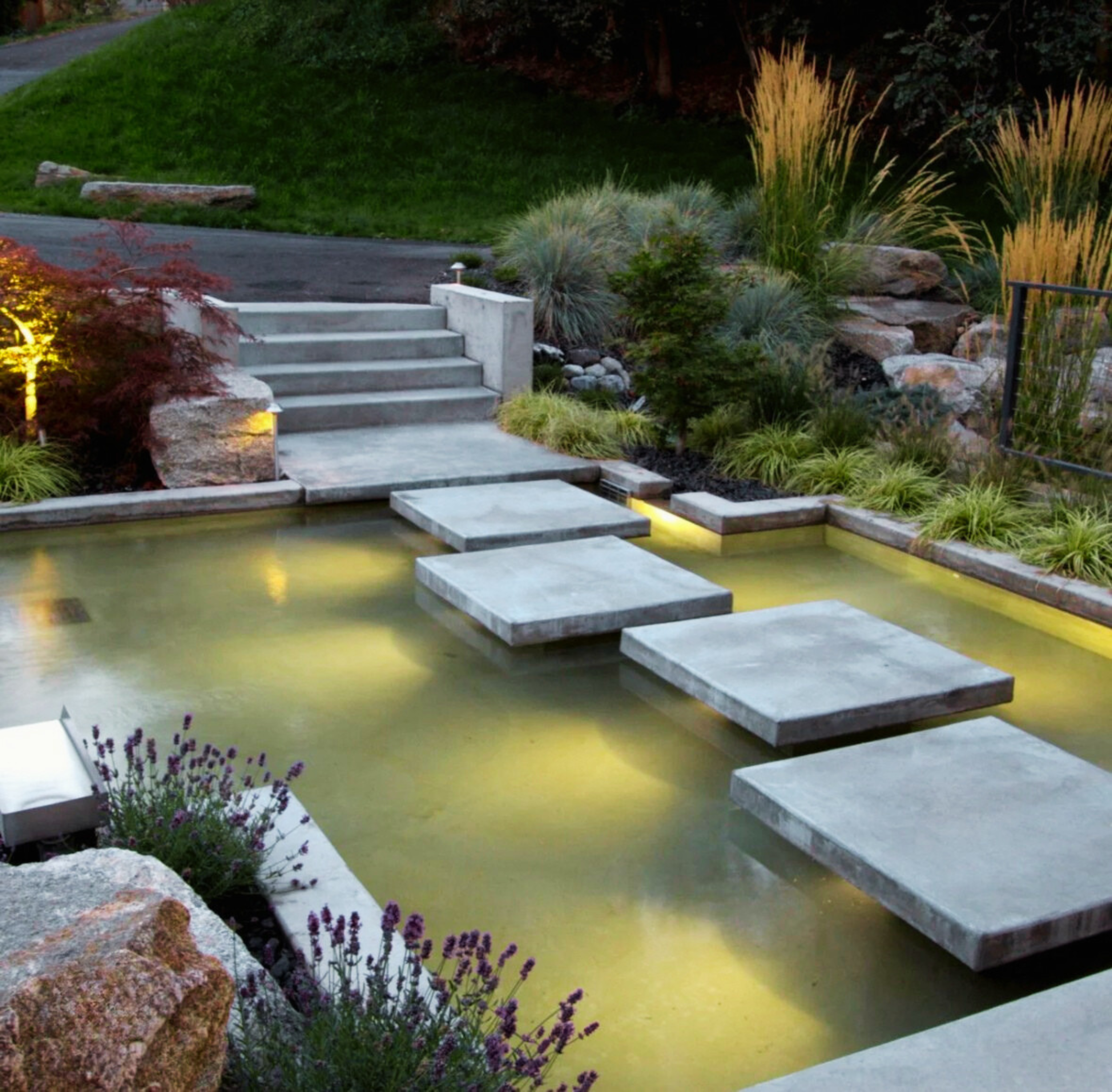 Modern floating concrete steps over a reflective water feature with integrated LED lighting, showcasing the precision structural craftsmanship of Cascades Dallas.