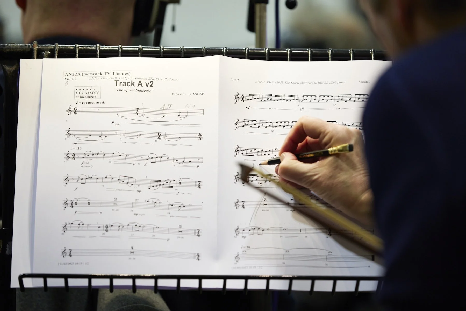 Une partition musicale pour violon intitulée 'The Spiral Staircase' avec une personne qui écrit ou ajuste la musique, vue de dos.