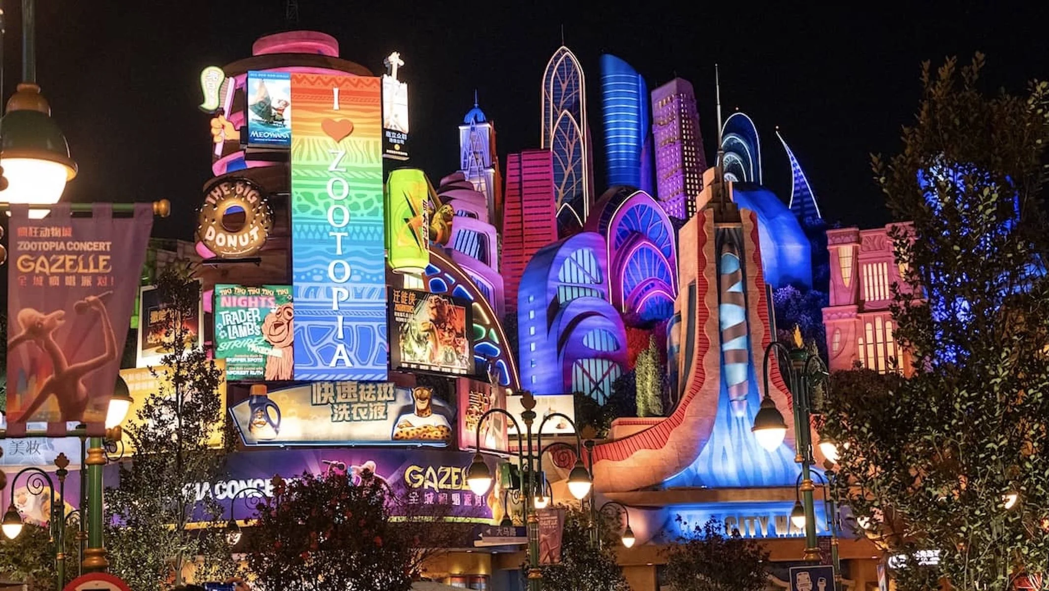 Un bâtiment futuriste avec des façades colorées illuminées, publicités en anglais et chinois, et une grande signification ZOOTOPIA. Il semble faire partie d'un parc d'attractions ou d'un spectacle nocturne.