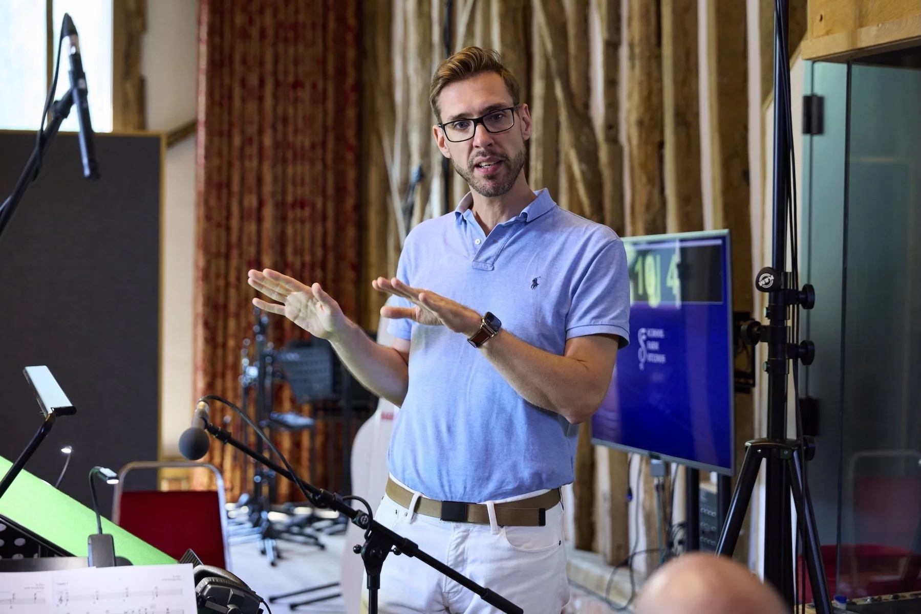 Un homme portant une chemise bleue et des lunettes parle lors d'une présentation ou d'une réunion dans un studio ou une salle de conférence.