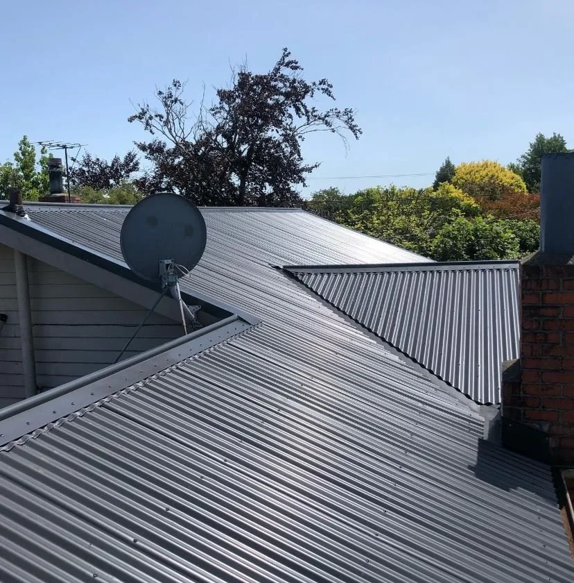 Metal roofing with a satellite dish on a house, trees in the background.