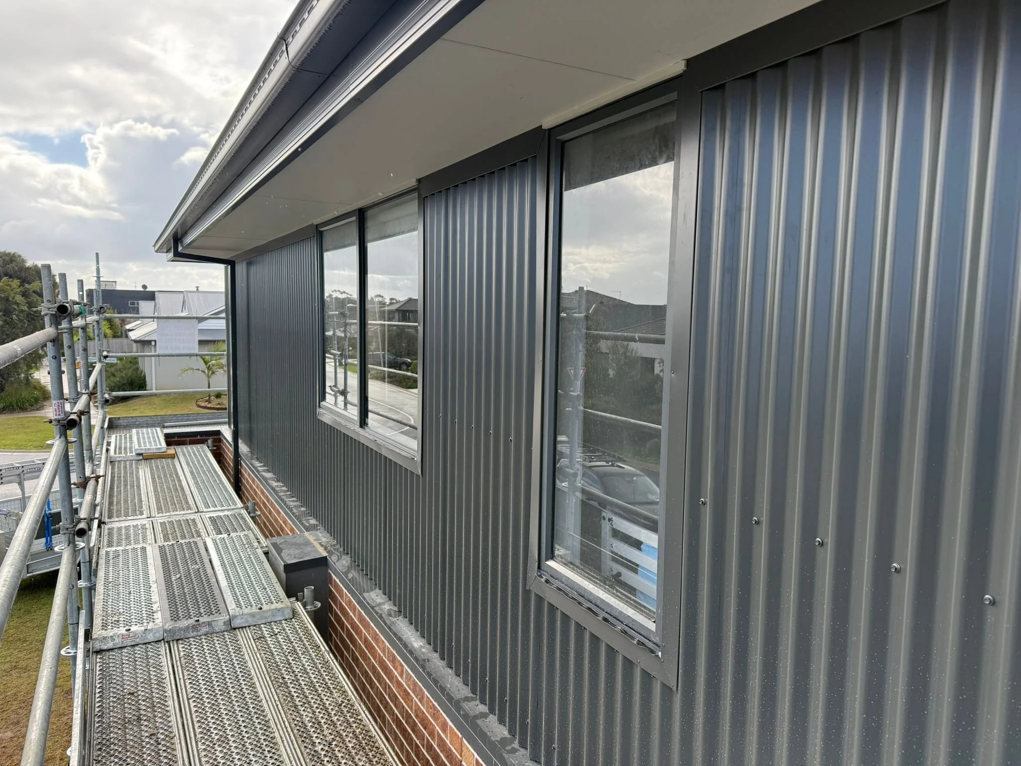 Construction scaffolding outside a building with corrugated metal siding and large window.
