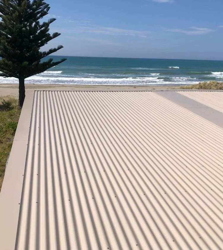 A corrugated metal roof with a coastal scene of the ocean and sky in the background, a tree to the left, and sandy beach nearby.