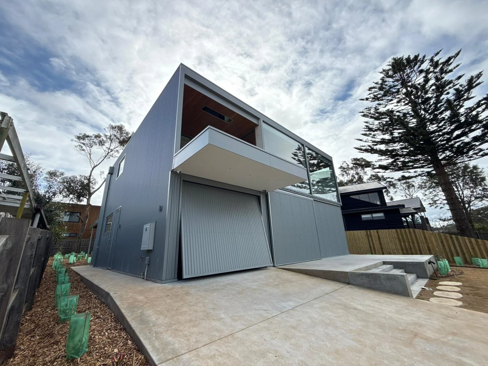 Modern two-story house with corrugated metal exterior, large glass windows, and a small front staircase with concrete steps leading to the entrance.