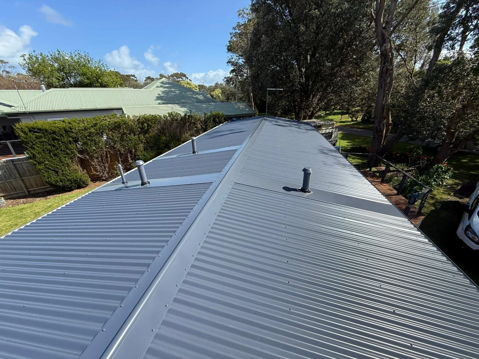 View of a metal roof with vents, surrounded by trees and neighboring houses.