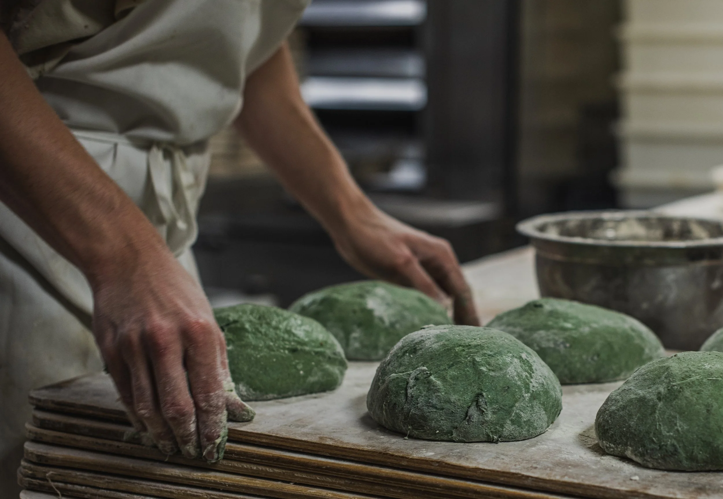 A person working with green dough or clay on a textured surface with rocks or stones, possibly in a kitchen or workshop setting.