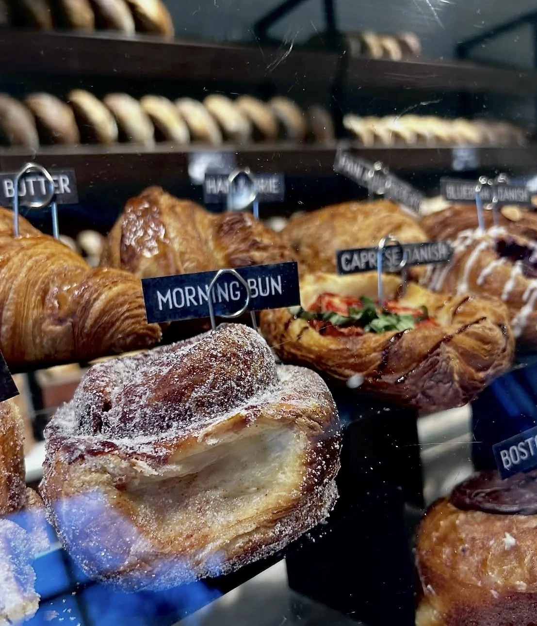 Display case with assorted baked goods including a sugar-dusted morning bun, croissants, and pastry with toppings.