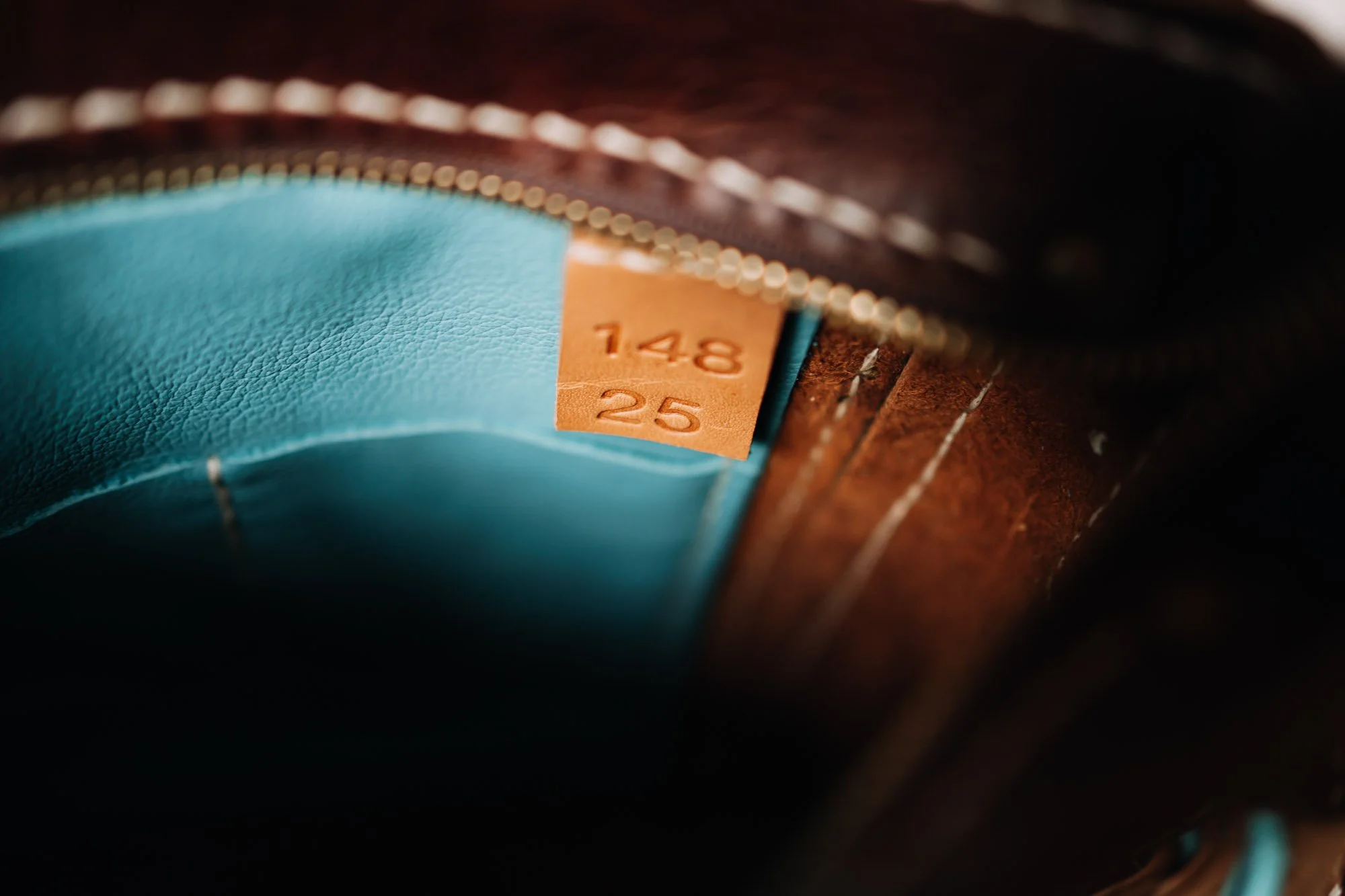 Close-up of the inside of a brown leather shoe, showing a size tag marked '148' and '25,' with a blue insole and a zipper.