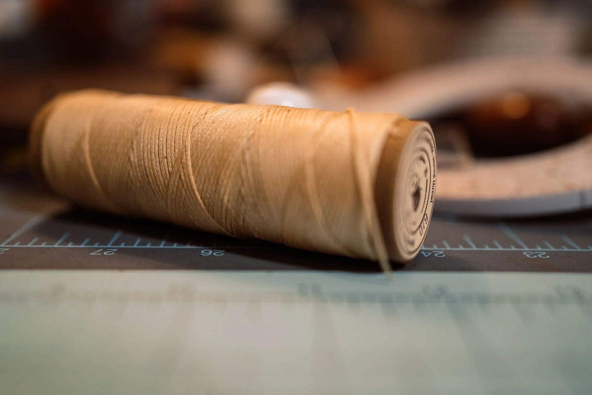 Close-up of a vintage wooden spool of thread lying on a cutting mat with measurement markings, with additional spools blurred in the background.