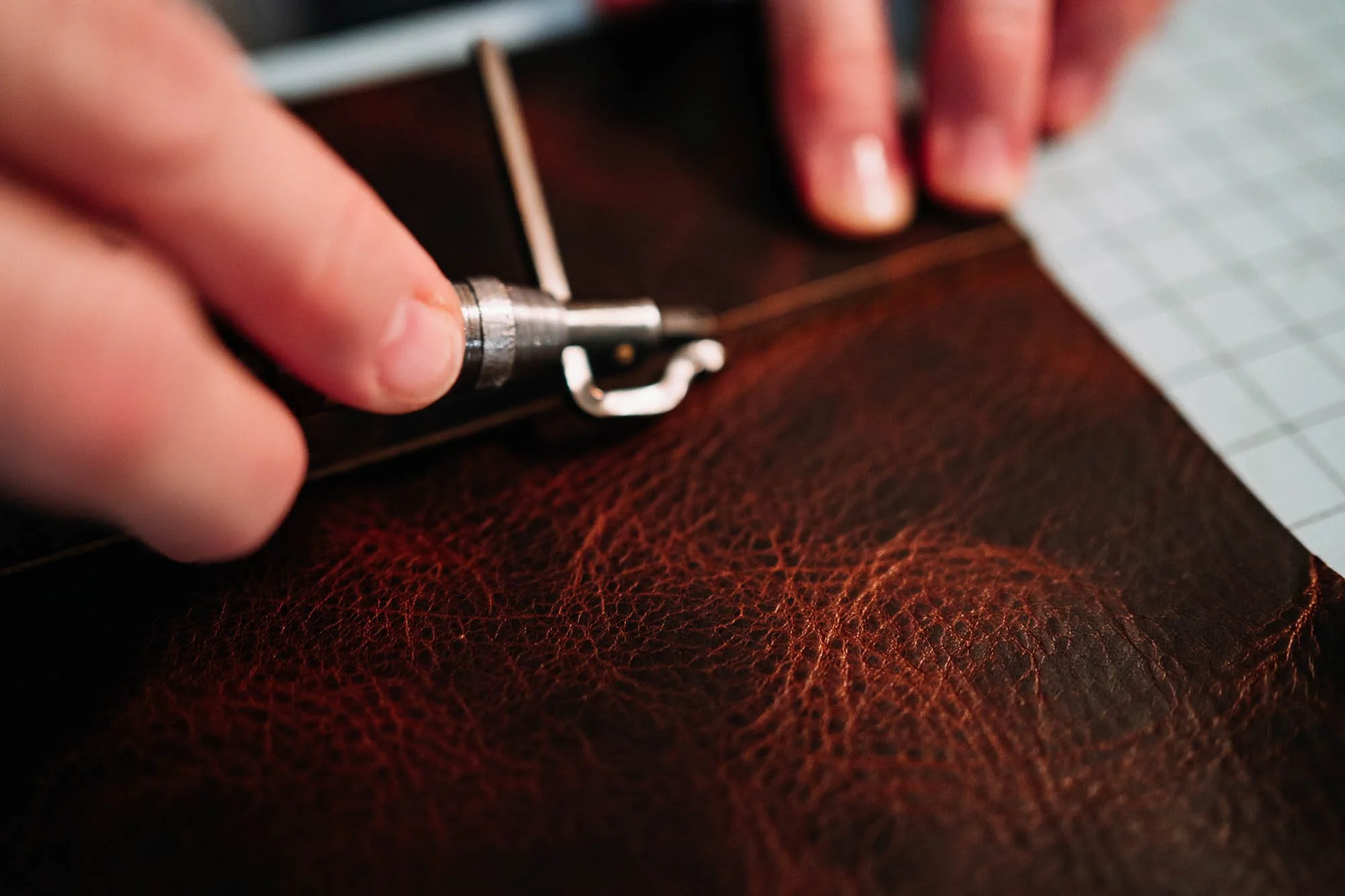 Close-up of a person using a rotary tool to craft or engrave brown leather.